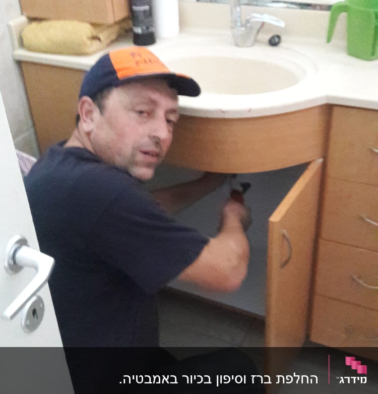 אדם מתקן צנרת מתחת לכיור בחדר אמבטיה